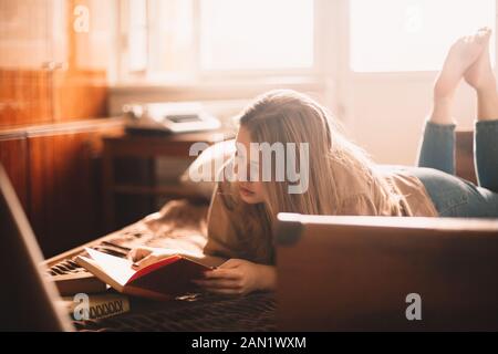 Libro di lettura della giovane donna mentre sdraiato sul letto a casa Foto Stock