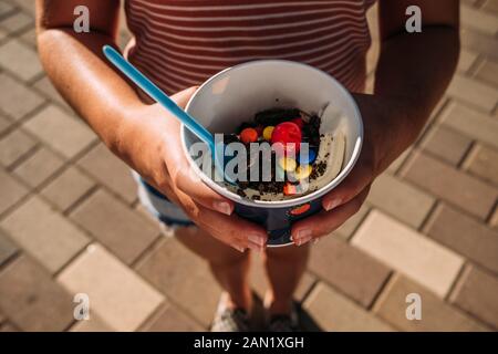 Vista ad alta angolazione di una ragazza che tiene una ciotola di gelato con condimenti Foto Stock
