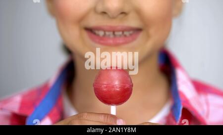 Ragazza adolescente che mostra lollipop in telecamera, cure dentarie concetto lo zucchero causa carie Foto Stock