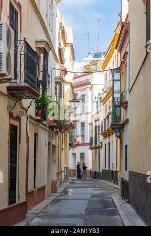 Edifici colorati fiancheggiano una strada stretta e tortuosa a Siviglia. Foto Stock