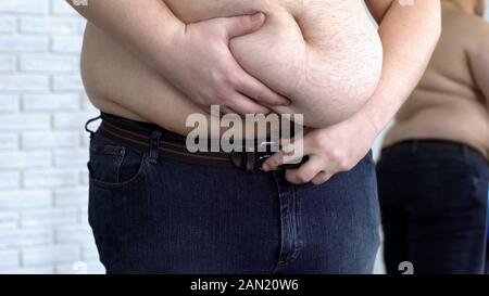 Uomo Oversize tenendo il grasso nello stomaco durante il serraggio della cinghia di jeans, disturbo metabolico Foto Stock