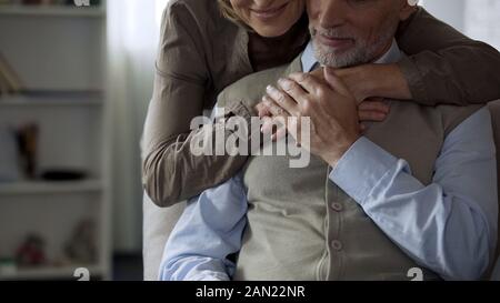 Signora anziana abbracciando il marito da dietro, relazioni amorevoli, tenerezza Foto Stock