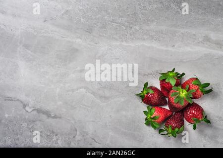 Una fotografia aerea di un intero fresche e mature di fragole organico su una luce di colore grigio pietra ardesia sfondo con spazio di copia Foto Stock