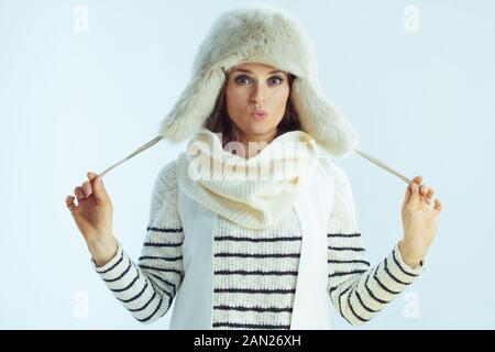 giovane donna in maglione a righe bianche, sciarpa e cappello con alette per orecchie isolato su sfondo azzurro invernale. Foto Stock