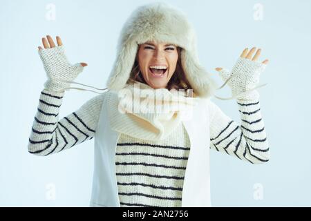 allegra donna moderna in maglione a righe bianche, sciarpa e orecchie con cappello che saltano isolato su sfondo azzurro invernale. Foto Stock