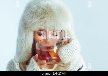 donna elegante in maglione a righe bianche, sciarpa e lembo auricolare cappello bere tazza di tè caldo con limone e miele su sfondo azzurro inverno. Foto Stock