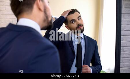 Giovane lavoratore di ufficio in business suit controllo taglio di capelli in riflessione a specchio Foto Stock