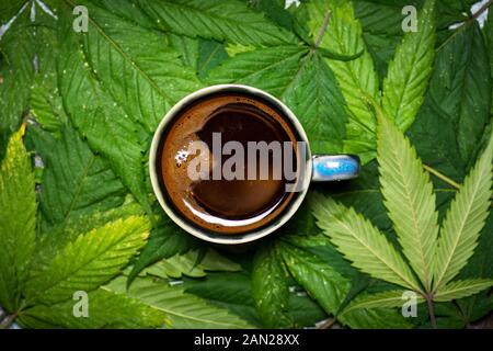 Una tazza di caffè sulla marijuana lascia il motivo di fondo Foto Stock