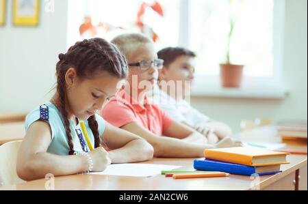 Felice scolari di studiare e rispondere alle domande in classe durante una lezione presso la scuola primaria Foto Stock