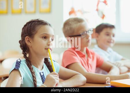 Felice scolari di studiare e rispondere alle domande in classe durante una lezione presso la scuola primaria Foto Stock