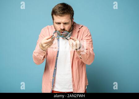 Scioccato, strano uomo barbuto detiene bicchieri in mani e con ansia esamina una lente. Foto Stock