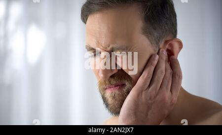 Uomo con il suo orecchio dolorante, che soffrono di otiti, improvvisa perdita di udito, close up Foto Stock