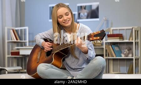 Signora giovane a suonare la chitarra nella sua stanza, la scrittura di canzone, sognando di carriera musicale Foto Stock