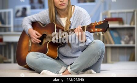 Musicista femmina accordare la chitarra sul divano di casa, godendo di melodia, pratica Foto Stock