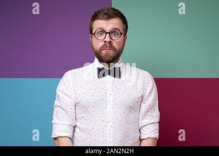 Strano, eccitato uomo barbuto in bicchieri arrotondati e un filtro bow tie, sta fermo e guarda nella telecamera con grandi occhi Foto Stock