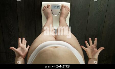 Il sovrappeso ragazza con grasso ventre permanente sulla bilancia, parola guida su schermo, arrabbiato Foto Stock