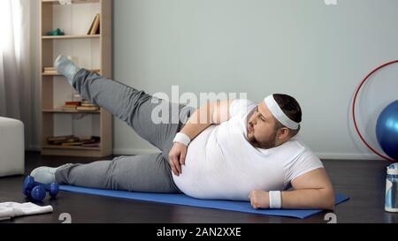 Maschi obesi gamba sollevamento disteso sul tappetino, uno stile di vita sano, sport tempo libero, esercizi Foto Stock