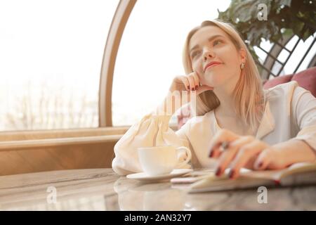 Sognante giovane donna a scrivere i piani futuri e gli obiettivi nel proprio diario di riposo in una accogliente caffetteria Foto Stock