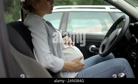 Donna incinta profondamente la respirazione, seduti in auto, sentirsi meglio dopo i dolori di pancia Foto Stock