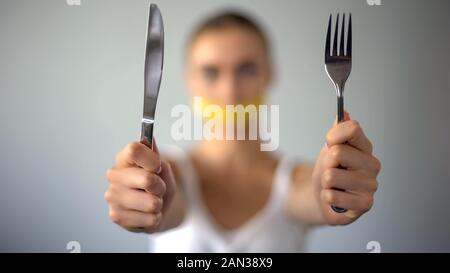 Ragazza con coltello e forchetta, bocca chiusa con nastro, restrizione di cibo, dieta Foto Stock