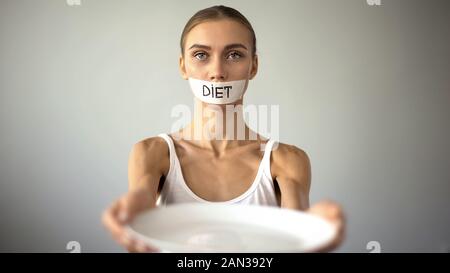 Slim ragazza con bocca con nastro adesivo che mostra la piastra a vuoto, dieta severa e di auto-distruzione Foto Stock