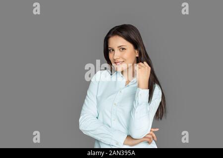 Freestyle. Giovane donna in piedi isolato su grigio in posa per fotocamera a sorridere gioiosa Foto Stock