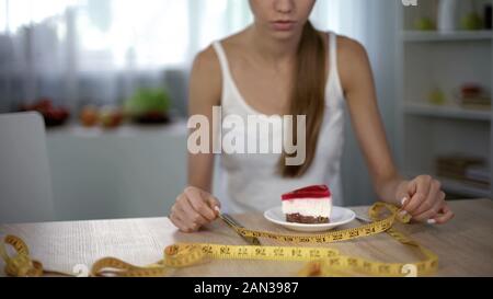 Ragazza la misura pezzo di torta con nastro adesivo, la paura di ingrassare, restrizione alimentare Foto Stock