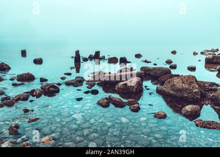 Lago di Bohinj nebbioso alba, rocce in acque poco profonde del lago glaciale in Slovenia Foto Stock