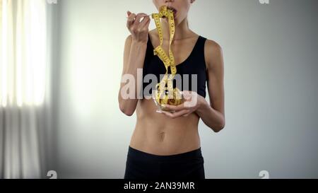 Ragazza Fitness mangiare nastro di misurazione, il concetto di controllo di BMI, restrizioni alimentari Foto Stock
