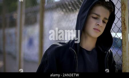 Ragazzo in hoodie appoggiata sul recinto, orfano in Boarding School di confinamento Foto Stock
