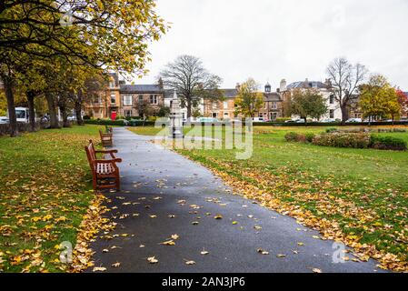 Giardino con un viale con panche di legno e di alberi decidui in un quartiere residenziale in un nebbioso giorno di autunno Foto Stock