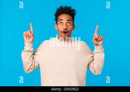 Wow impressionante. Impressionato bello ragazzo africano con baffi e capelli afro, piegatura labbra sorridente e fissando, rivolto verso l'alto a incredibili mozzafiato Foto Stock