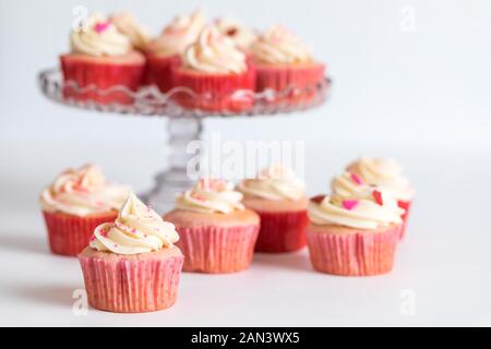 Tortini di fragola con la glassa di formaggio cremoso su una torta stand con più sul tavolo di fronte per il giorno di San Valentino. Foto Stock