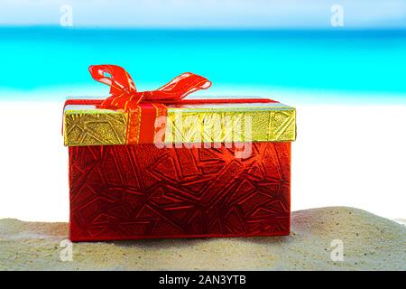 Confezione regalo rossa sulla sabbia di mare. Concetto di regalo per il giorno di San Valentino, Wedding, Natale o Estate vacanza tropicale. Foto Stock