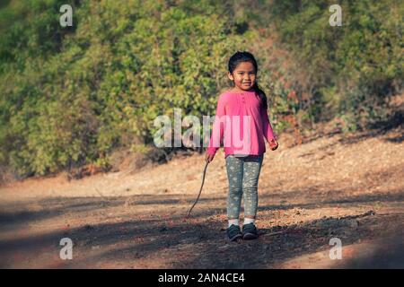 Ragazza giovane indossando maglia rosa che cammina da sola in un sentiero escursionistico tenendo un bastone di legno in mano. Foto Stock