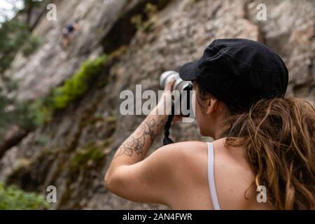 Un oltre la spalla di un fotografo sportivo al lavoro. come una donna usa fotocamera professionale e un teleobiettivo per fotografia sfocata rocciatore Foto Stock