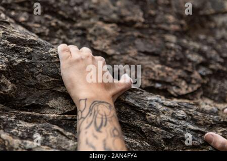 Libera assolo rock climbing in natura, una tecnica in cui advanced scalatore rupe di scale senza dispositivi di sicurezza, tatuato il braccio e la mano afferra la pietra Foto Stock