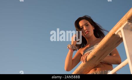 Asian teen in tube top appoggiato su ringhiera e tenendo i capelli, mentre incorniciato con cielo blu su traghetto barca andare a Lesvos Foto Stock