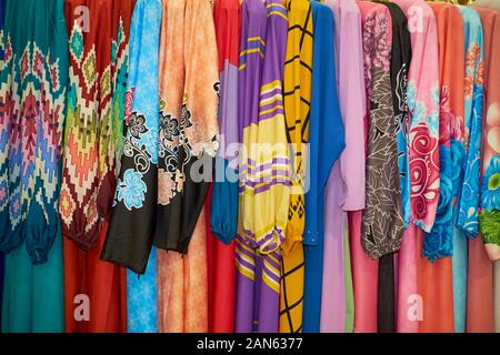 Una cremagliera di colorati, forte, tradizionale design Malay abiti in tessuto. In corrispondenza di un tessuto, negozio di abbigliamento nel centro cittadino di Kuala Lumpur, Malesia. Foto Stock