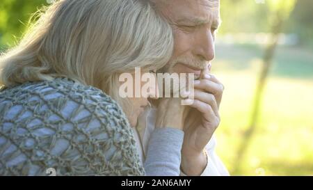 Vecchia donna sostenere e abbracciando il suo pianto ill marito, cattive notizie, disperazione Foto Stock
