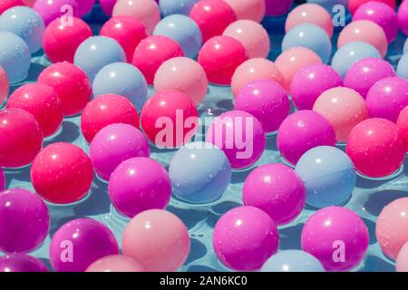 Primo piano di palline colorate di plastica che nuotano in acqua. Concetto / astratto per partito, essere felice, essere in una squadra o diversità. Foto Stock