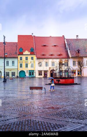 Sibiu, Romania - Marzo 27, 2015: Case con il famoso conformata ad occhiello windows sui tetti e le persone a piazza principale Foto Stock