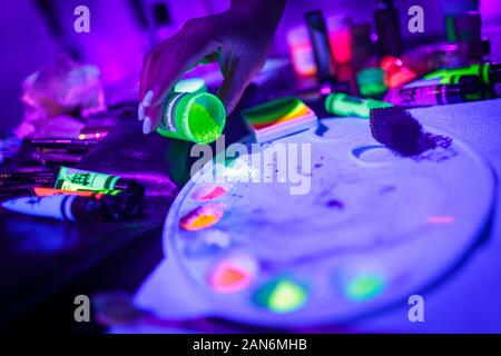 Polvere fluorescente UV multicolore e vernici su una tavolozza Foto Stock