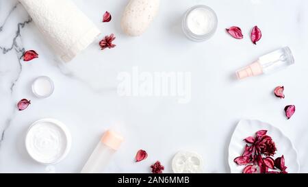 Prodotti di Cosmetica Naturale e petali di rosa su sfondo marmo. Cornice fatta di asciugamani, sapone artigianale, oli essenziali, spugna Luffa, Crema mani. Lay piatto Foto Stock