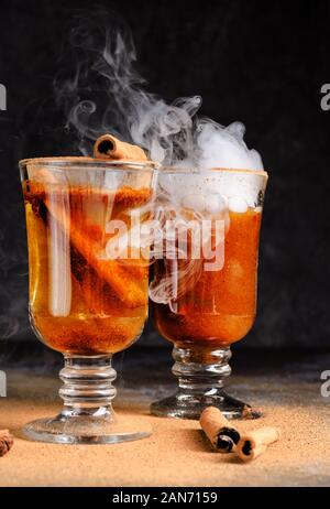 Vin brulé alla cannella in bere due bicchieri di vetro con vapore bianco. Dark moody cibo ancora in vita. Foto Stock