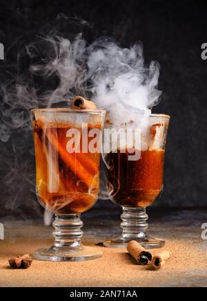 Vin brulé alla cannella in bere due bicchieri di vetro con vapore bianco. Dark moody cibo ancora in vita. Foto Stock