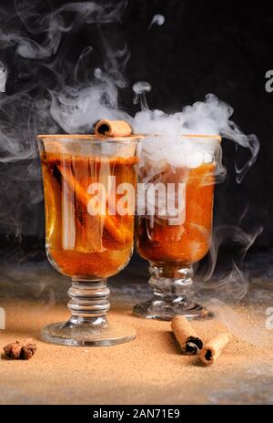 Vin brulé alla cannella in bere due bicchieri di vetro con vapore bianco. Dark moody cibo ancora in vita. Foto Stock