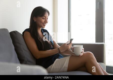 Sorridente dipendente asiatici relax in ufficio avente piacevole parlare al cellulare Foto Stock