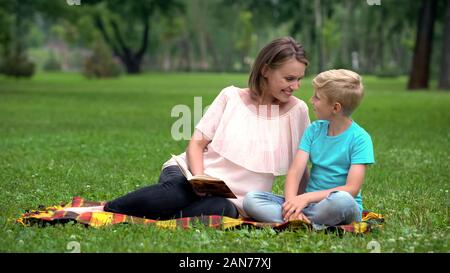 Il figlio e la madre la lettura interessante avventura prenota, seduti su una coperta in posizione di parcheggio Foto Stock