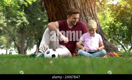 Padre figlio guardando un gioco su tablet, intrattenimento di generazione digitale Foto Stock